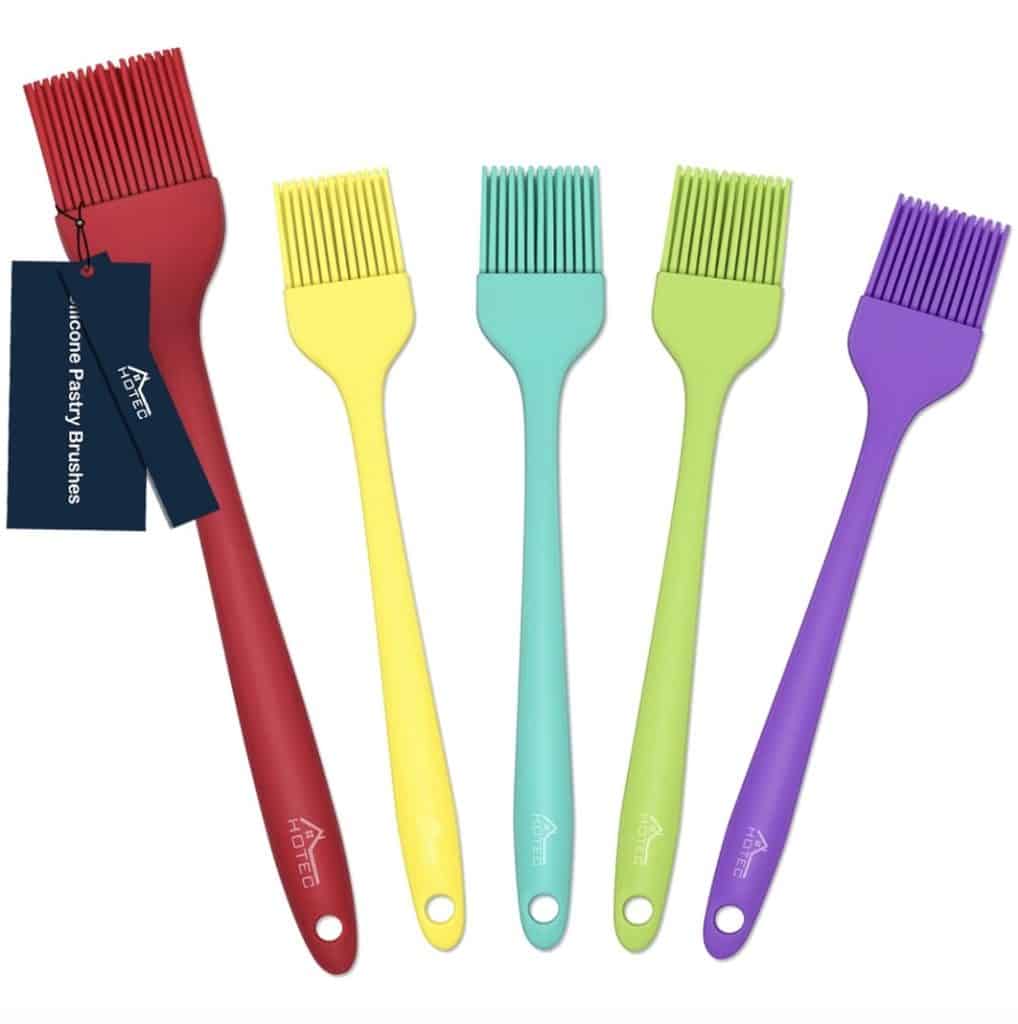 Five colorful silicone pastry brushes, perfect for that infused chicken recipe, are arranged vertically side by side. The brushes come in red, yellow, teal, green, and purple, each with a branded handle and a tag attached to the red brush.